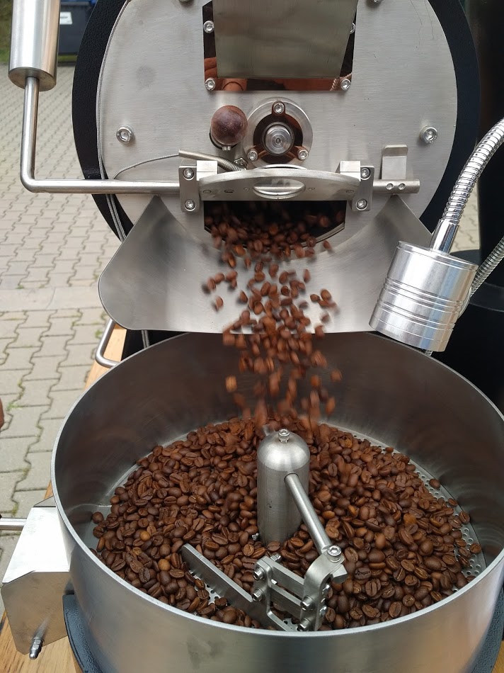 Kaffeebohnen fallen aus dem Trommelröster ins Kühlsieb